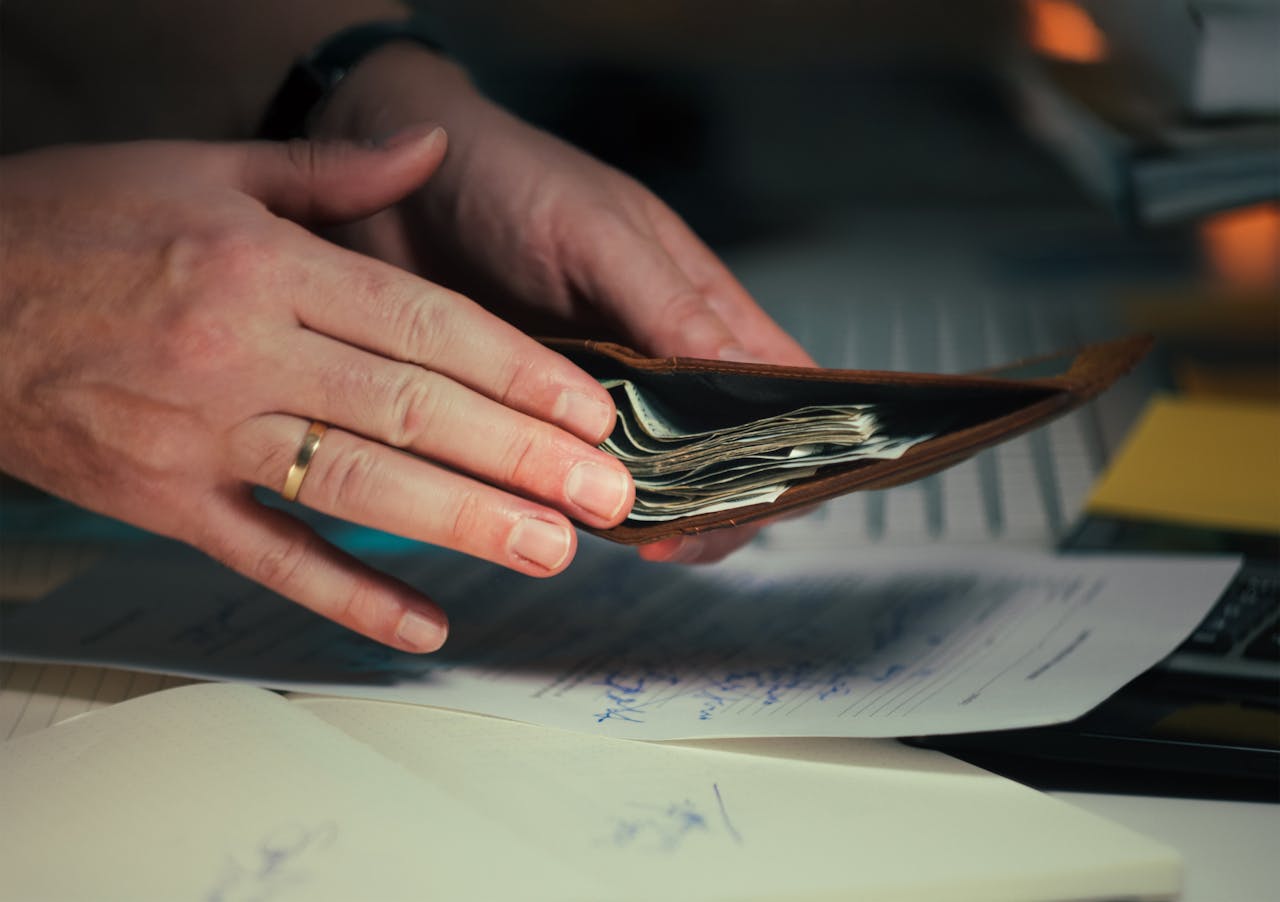 services-01 Hands holding an open wallet filled with cash above documents, indicating financial planning or budgeting.